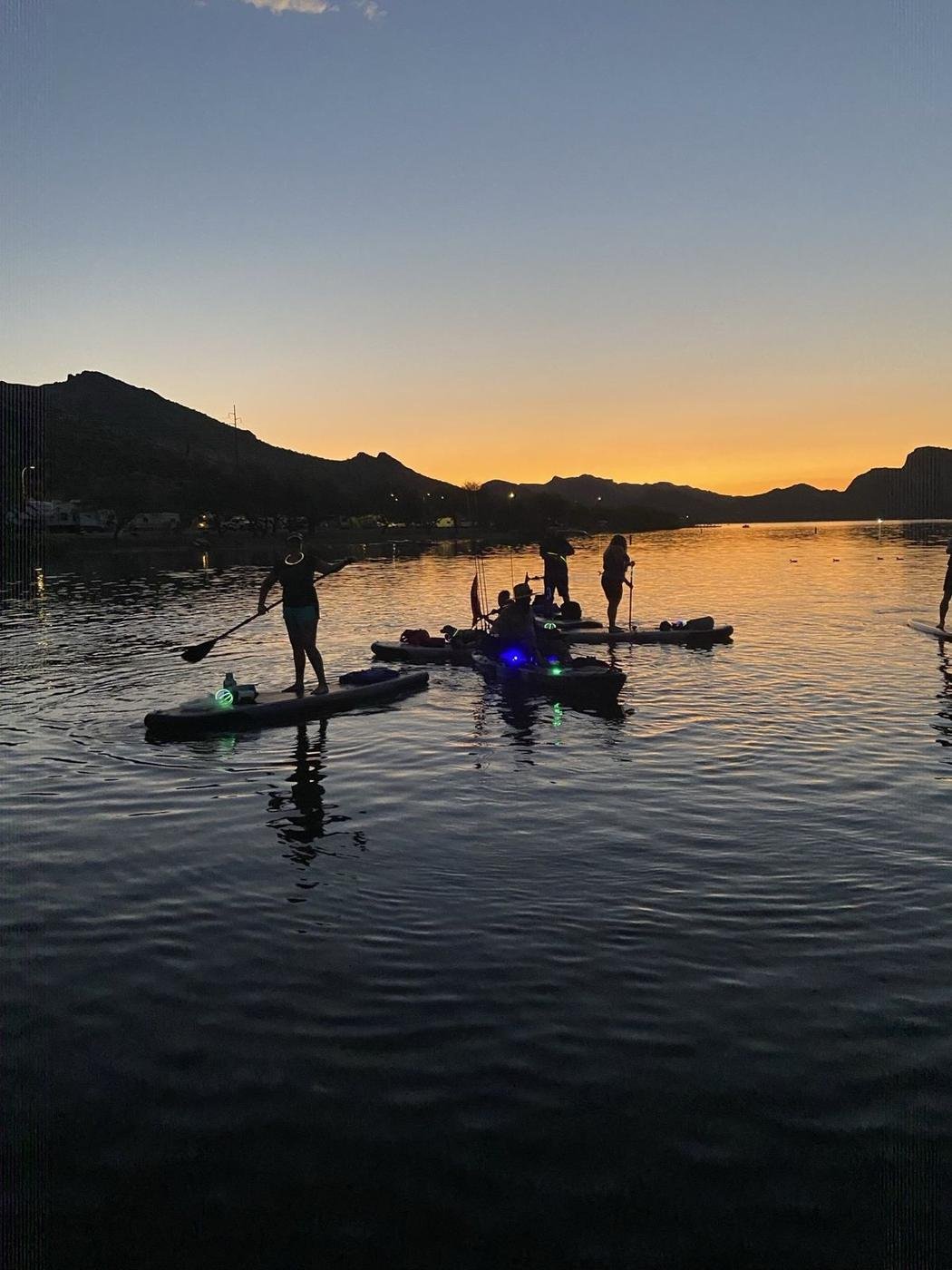Paddleboarders and kayakers with glow sticks at dusk on Saguaro Lake